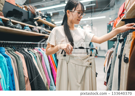 Young adult woman choosing used clothing at second hand clothes shop 133640370