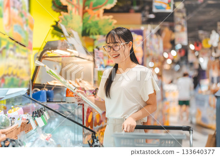 Young adult asian woman consumer choosing vegetable food products at supermarket store choice buying 133640377