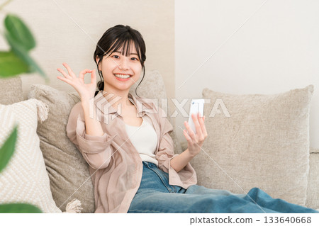 Asian woman using smartphone app while sitting on sofa in living room (ok, nice, like, good) Asian woman using smartphone app while sitting on sofa in living room (ok, nice, like, good) 133640668