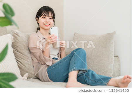 亞洲女子坐在客廳沙發上使用智慧型手機應用程式 133641490