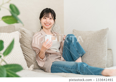 亞洲女子坐在客廳沙發上使用智慧型手機應用程式 亞洲女子坐在客廳沙發上使用智慧型手機應用程式 133641491
