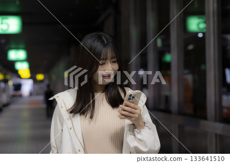 A woman looking at her smartphone at a station or bus terminal late at night A woman looking at her smartphone at a station or bus terminal late at night 133641510