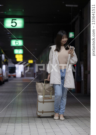 Women's commute to work and home scenes looking at their smartphones at city stations, airports, and bus terminals at night, and urban lifestyles. Full body Women's commute to work and home scenes looking at their smartphones at city stations, airports, and bus terminals at night, and urban lifestyles. Full body 133641511