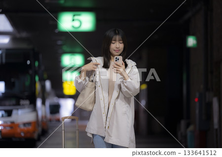夜晚，一位女性在城市車站、機場或汽車站通勤途中，低頭看著智慧型手機，展現了她的都市生活方式。 133641512
