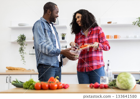 A smiling couple prepares a meal together in a bright, modern kitchen, filled with fresh ingredients. 133641580