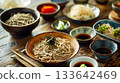 A table set for a traditional soba noodle feast with various toppings and dipping sauces in small dishes 133642469