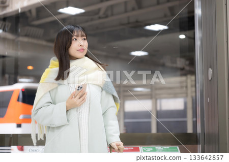 冬天，一位女士在火車站台或汽車站揮手致意，她手裡拿著智慧型手機。 133642857