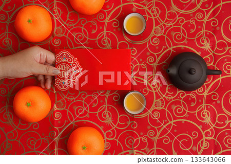 Chinese New Year Celebration. Hand holding red envelope with oranges and tea. 133643066