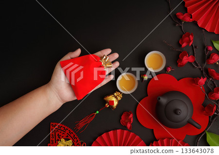 Chinese New Year Celebration. Hand holding red envelope with tea and decorations. Chinese New Year Celebration. Hand holding red envelope with tea and decorations. 133643078