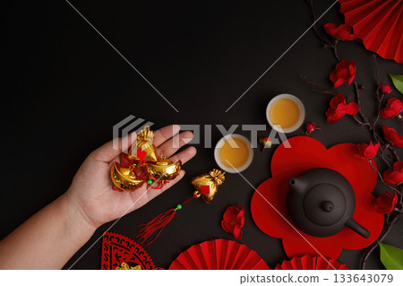 Chinese New Year. Hand holding gold ingots with tea and festive decor. 133643079