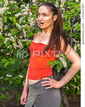 Young woman sneezes in the park against the background of a flowering tree. Allergy to pollen concept. Young woman sneezes in the park against the background of a flowering tree. Allergy to pollen concept. 133643467