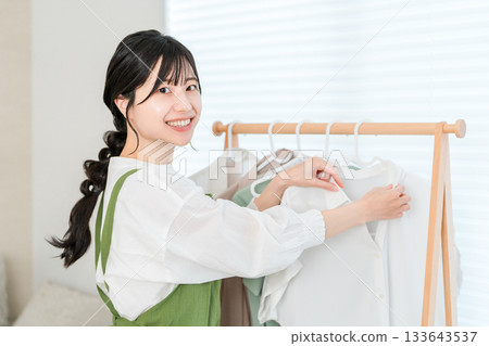 Asian housewife woman doing housework hanging clothes on hangers on clothes rack Asian housewife woman doing housework hanging clothes on hangers on clothes rack 133643537