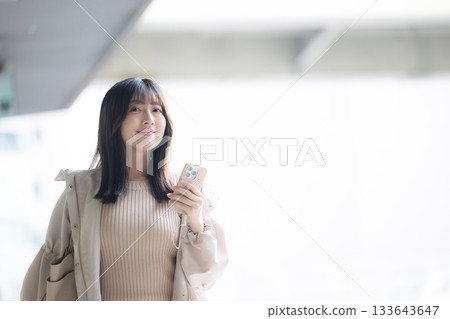 一張照片，照片中一名女子在機場或大眾運輸樞紐站手持智慧型手機，背景中可以看到一架飛機。 133643647