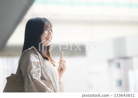 Photo of a woman holding a smartphone at an airport or transportation terminal. Travel and holiday image. Profile. 133643651