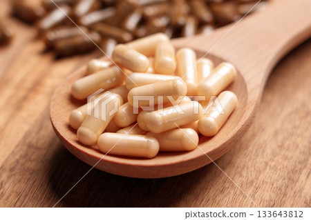 Different vitamin pills placed in wooden spoon and scattered on brown plank board close up Different vitamin pills placed in wooden spoon and scattered on brown plank board close up 133643812