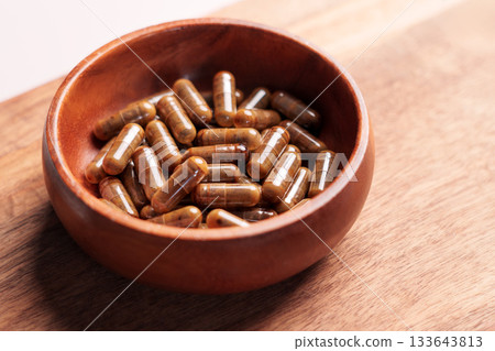 Brown vitamin capsules in wooden bowl on plank board. Natural herbal supplements Brown vitamin capsules in wooden bowl on plank board. Natural herbal supplements 133643813