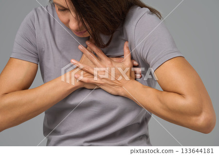 Close-up of woman clutching chest in pain, eyes closed, expressing discomfort  133644181