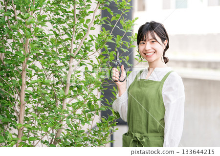 A housewife in an apron pruning garden trees with pruning shears 133644215