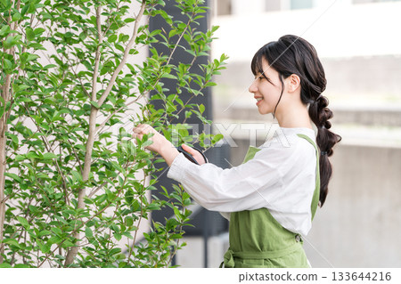 A housewife in an apron pruning garden trees with pruning shears 133644216