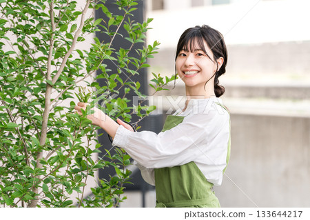 A housewife in an apron pruning garden trees with pruning shears 133644217