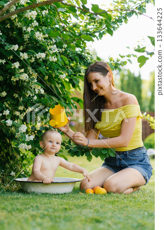 Mother and Baby Playing with Watering Can in Garden Mother and Baby Playing with Watering Can in Garden 133644225
