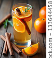 Spiced winter beverage with orange slices, cinnamon sticks, and rosemary garnish in a glass on a rustic wooden table. Spiced winter beverage with orange slices, cinnamon sticks, and rosemary garnish in a glass on a rustic wooden table. 133644458