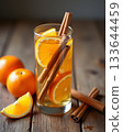 Spiced winter beverage with orange slices, cinnamon sticks, and rosemary garnish in a glass on a rustic wooden table. Spiced winter beverage with orange slices, cinnamon sticks, and rosemary garnish in a glass on a rustic wooden table. 133644459