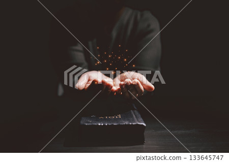 Open hand with glowing light above the Holy Bible, symbolizing prayer, blessing, faith, Christianity, divine hope and spiritual strength from God Word and holy guidance. 133645747