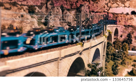 Miniature blue train crossing stone viaduct in model landscape Miniature blue train crossing stone viaduct in model landscape 133645756