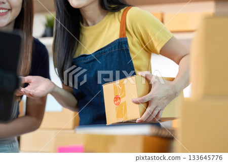 E-commerce. Woman holding a package while discussing with a colleague in a modern workspace. E-commerce. Woman holding a package while discussing with a colleague in a modern workspace. 133645776