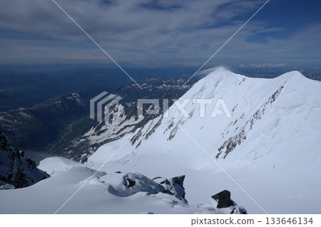 A stunning rock formation covered in snow, set against a clear blue sky with fluffy clouds in the background, creating a peaceful and breathtaking mountain landscape. 133646134