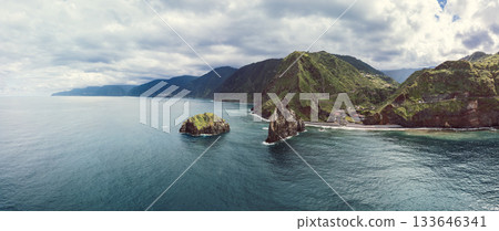 Panoramic drone Madeira Ribeira da Janela sea stacks rising from Atlantic beside lush green cliffs 133646341