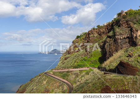 Curving road beneath Garajau cliffs toward Funchal beside green slopes and deep blue Atlantic 133646343
