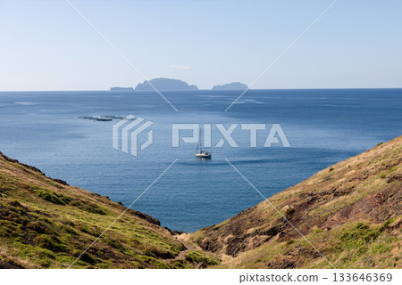 V shaped Sao Lourenco slopes descend to Atlantic where a lone sailboat floats under pale sky V shaped Sao Lourenco slopes descend to Atlantic where a lone sailboat floats under pale sky 133646369