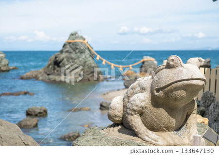 Meoto Iwa Wedded Rocks near Futami, Ise city, Japan, Stone frog statue near rocky coast with ocean and rope bridge in background 133647130