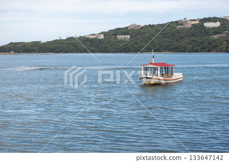 Ama Divers of Ise Shima fishing tradition in Mie Prefecture, Japan Small passenger boat cruising on calm water near coastal hillside with buildings 133647142