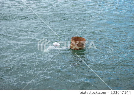 Ama Divers of Ise Shima fishing tradition in Mie Prefecture, Japan Wooden barrel floating in calm water with plastic bag pollution 133647144