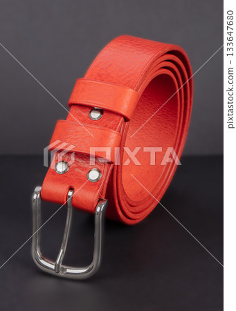 Red leather belt with metal buckles on a gray background. 133647680