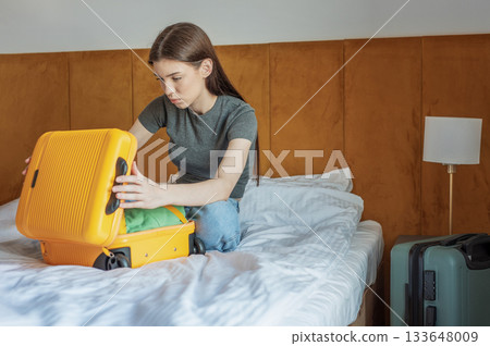 Young woman packing yellow suitcase on hotel bed 133648009