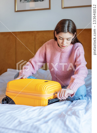 Woman packing yellow suitcase on bed for travel 133648012