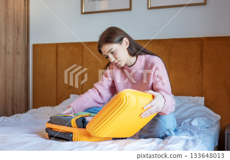 Young woman packing suitcase for upcoming travel journey Young woman packing suitcase for upcoming travel journey 133648013
