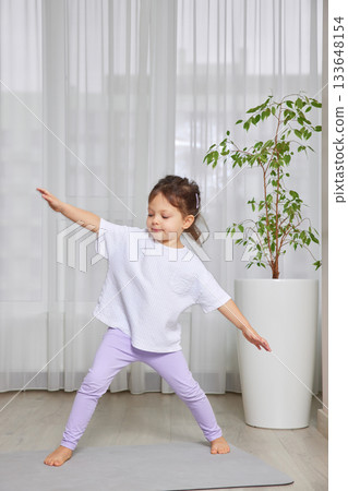 Young girl balancing and stretching on a yoga mat during indoor exercise 133648154