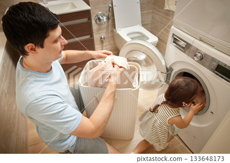 Father and daughter sorting clothes from the laundry basket in bathroom 133648173