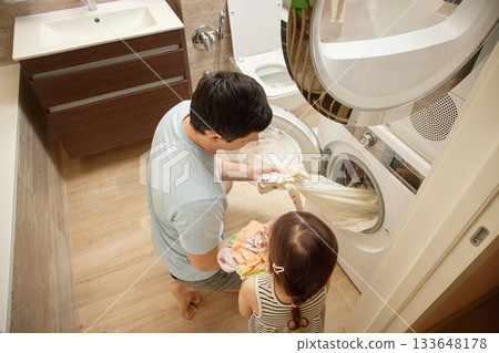 Father and daughter putting dirty clothes into a washing machine in the bathroom 133648178