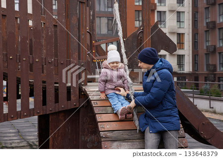 Father helping his daughter sliding down on a playground structure Father helping his daughter sliding down on a playground structure 133648379