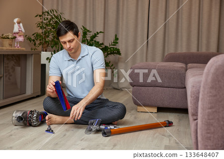 Man disassembling a cordless vacuum cleaner for maintenance in living room 133648407