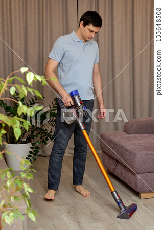 Man cleaning living room floor with a cordless vacuum cleaner Man cleaning living room floor with a cordless vacuum cleaner 133648508