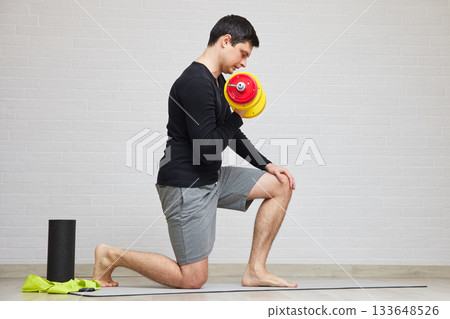 Man kneeling on a yoga mat lifting dumbbell for an arm workout Man kneeling on a yoga mat lifting dumbbell for an arm workout 133648526