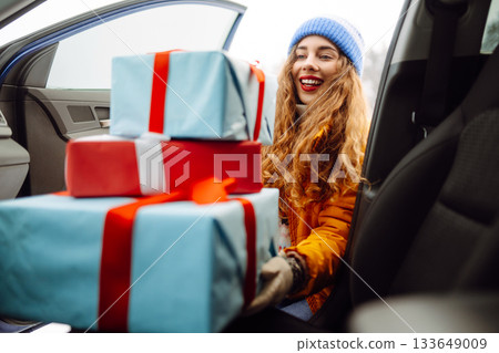 Happy young woman putting New Year's gifts into a car. The eve of the winter holidays, preparation. Happy young woman putting New Year's gifts into a car. The eve of the winter holidays, preparation. 133649009