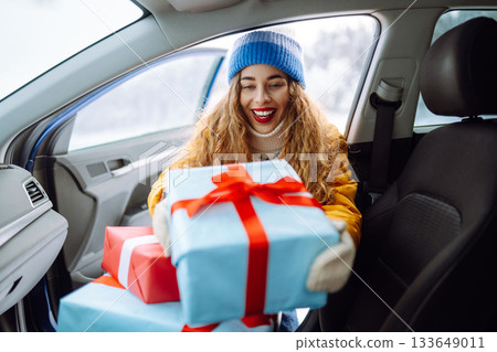 Happy young woman putting New Year's gifts into a car. The eve of the winter holidays, preparation. 133649011
